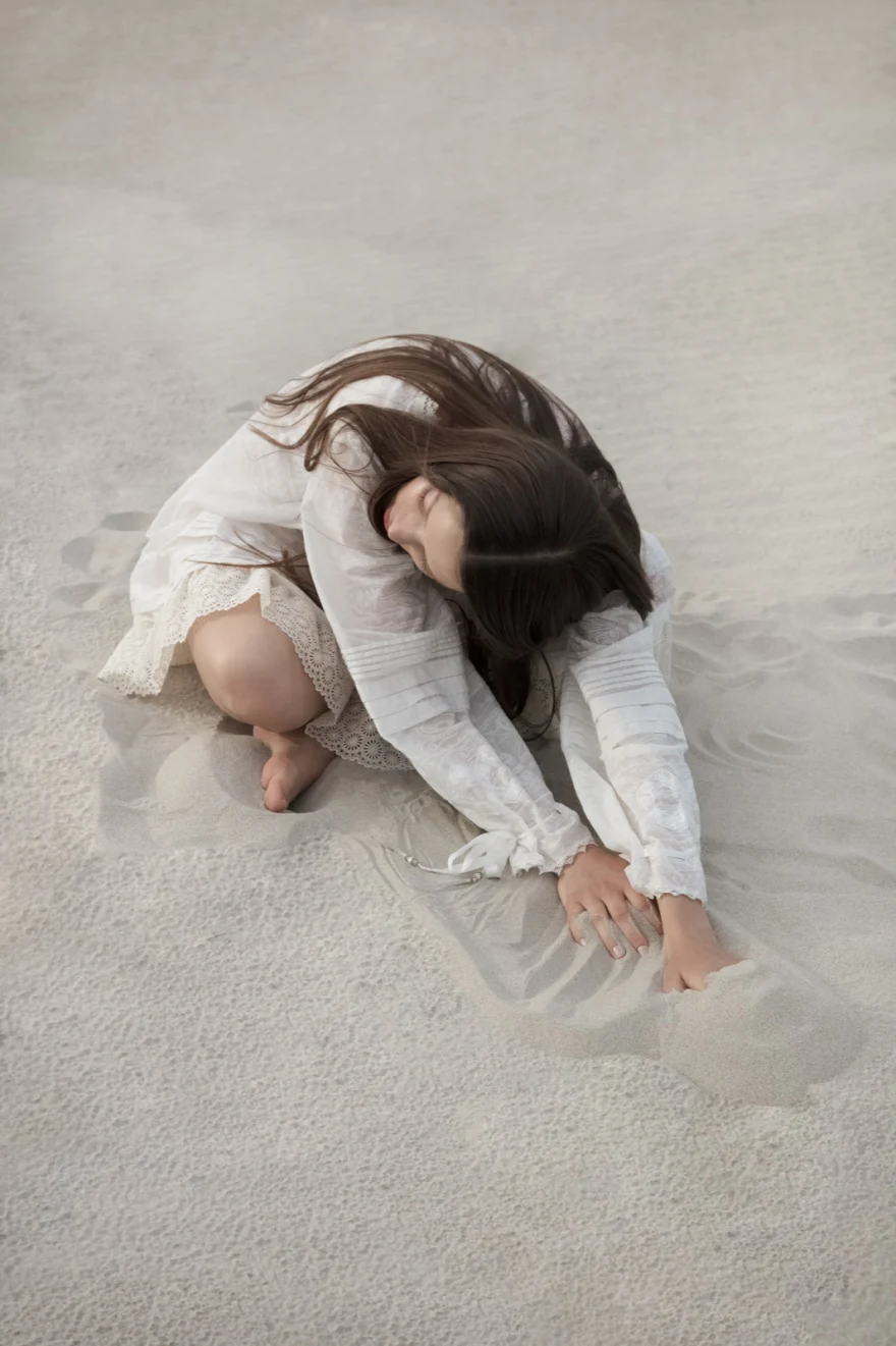 Model curled on white sand in a cream lace dress, ETRO × SHOT Magazine editorial photographed by Ina Cenusa