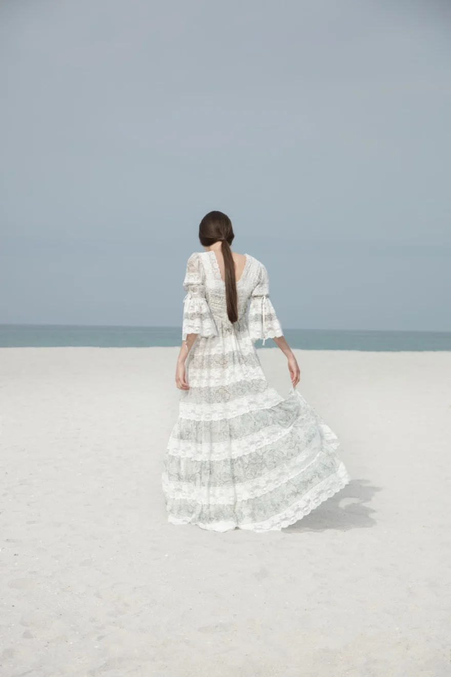 Back view of a tiered white lace gown on a pale sand beach, ETRO × SHOT Magazine editorial photographed by Ina Cenusa