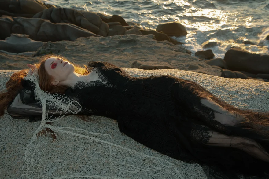 Model in black lace lying on the shore beside a fishing net at golden hour, SHOT Magazine editorial photographed by Ina Cenusa