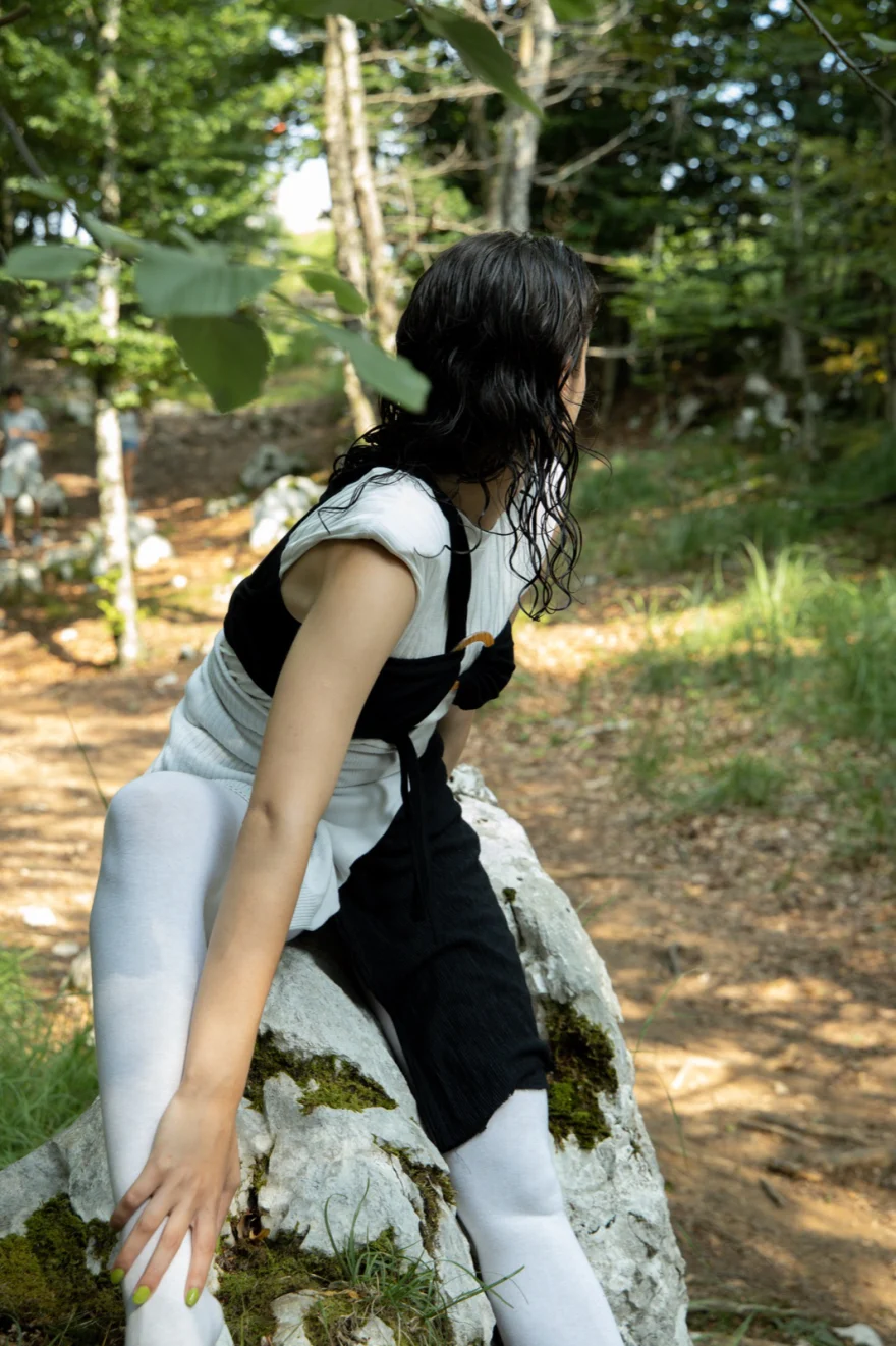 Model in a black and white look seated on a mossy rock in the woods, SHOT Magazine editorial photographed by Ina Cenusa