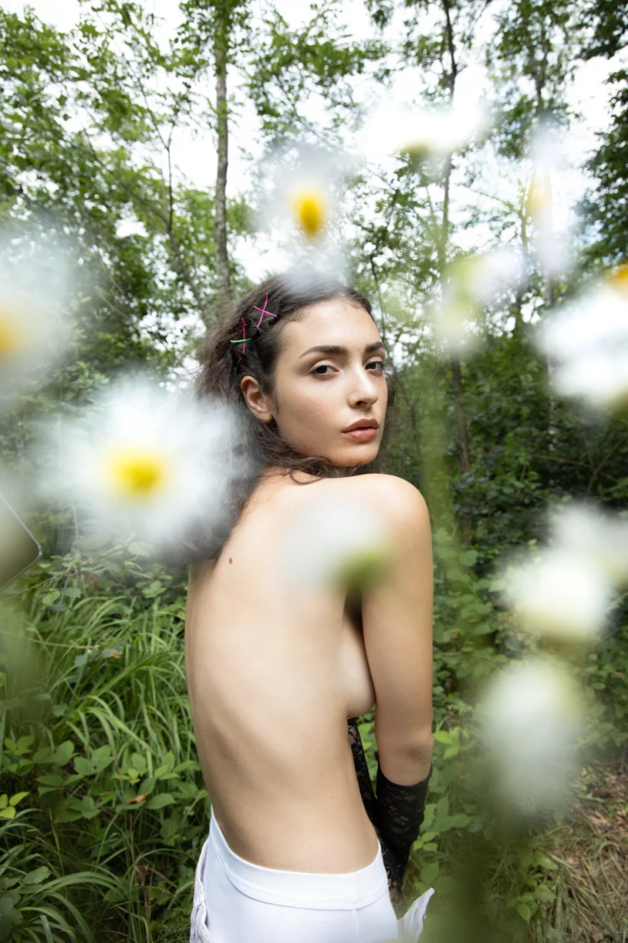 Model glancing back among daisies in woodland, SHOT Magazine editorial photographed by Ina Cenusa