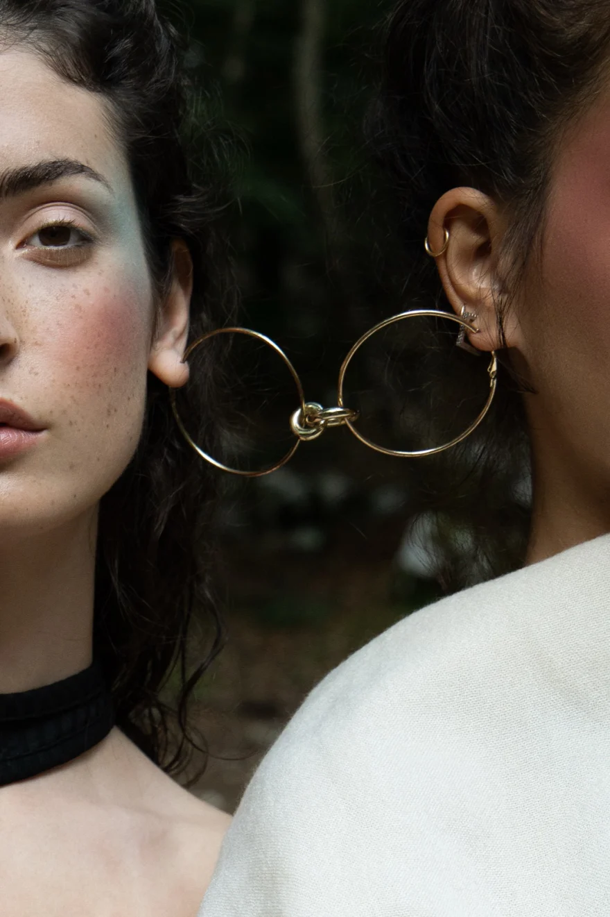 Two figures framed by large gold hoop earrings in the woods, SHOT Magazine editorial photographed by Ina Cenusa