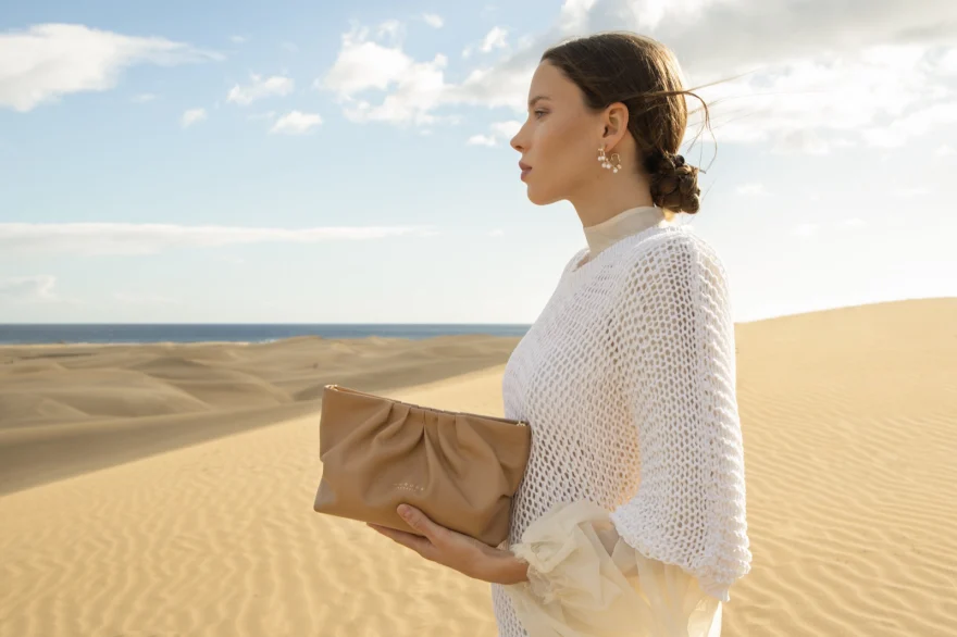 Profile of a model in white knitwear with a tan clutch on the Gran Canaria dunes, Aurora Venezia campaign photographed by Ina Cenusa