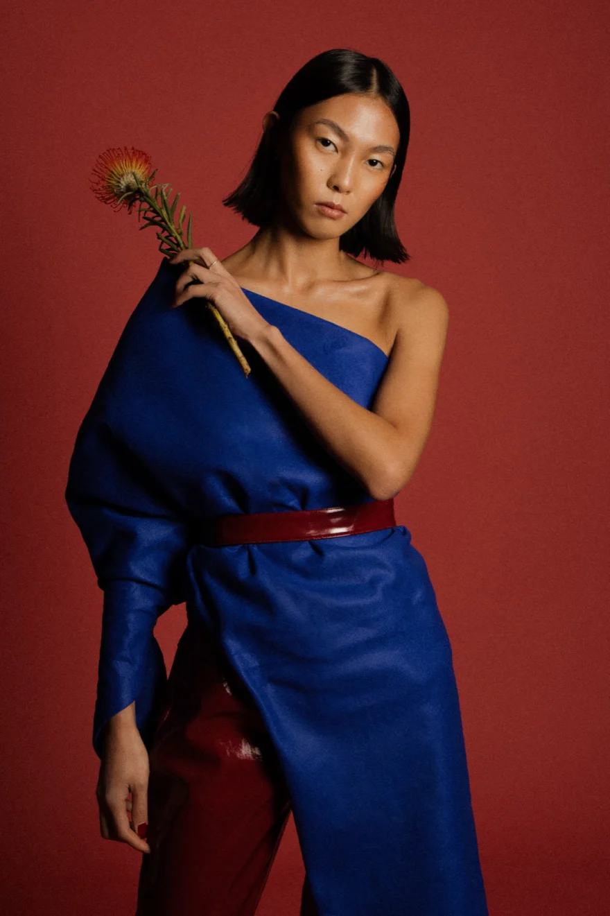 Model in a cobalt blue one-shoulder dress holding an orange protea flower, LYX Magazine editorial photographed by Ina Cenusa