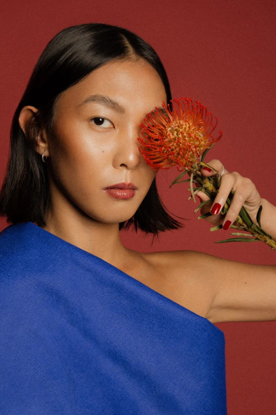 Portrait holding an orange flower beside the face, LYX Magazine editorial photographed by Ina Cenusa