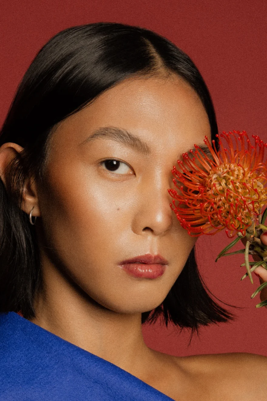 Beauty portrait with an orange flower covering one eye, LYX Magazine editorial photographed by Ina Cenusa