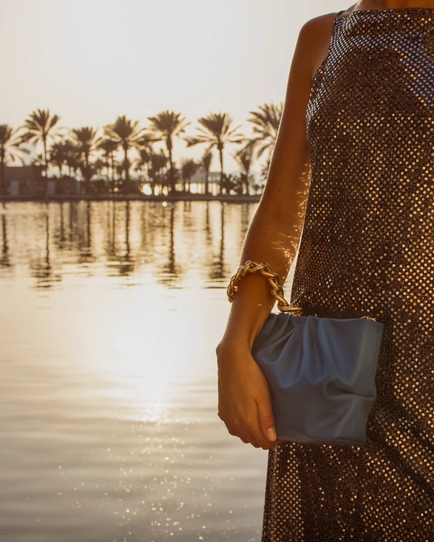 Detail of a pale blue bag held against the light, palms and water at sunset, Aurora Venezia campaign in Dubai photographed by Ina Cenusa