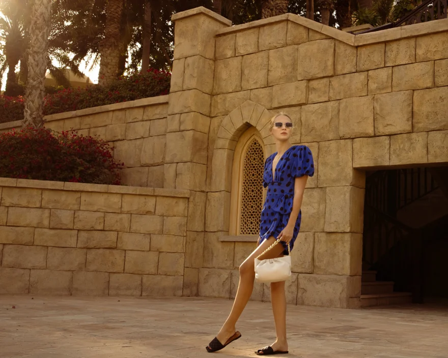 Wide shot of the model in a blue printed dress against sandstone architecture, Aurora Venezia campaign in Dubai photographed by Ina Cenusa
