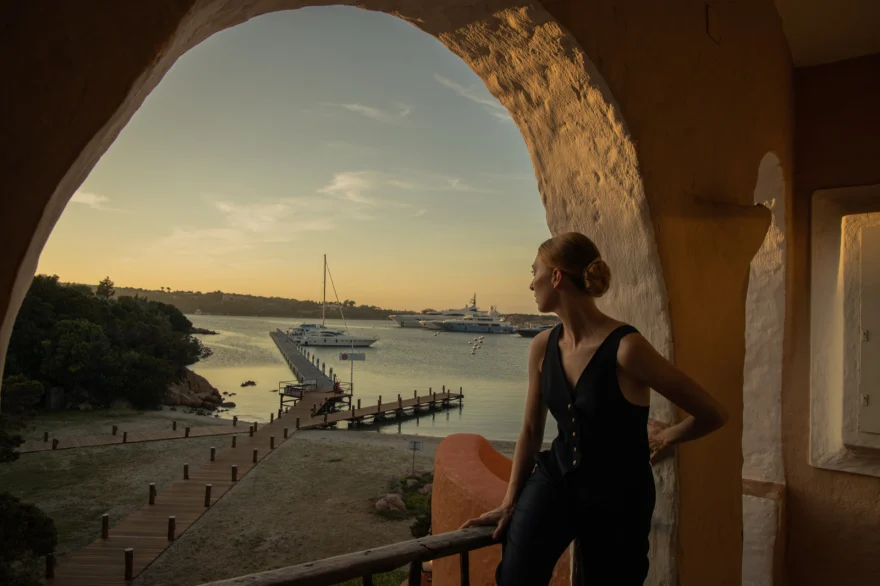Model framed by a stone arch overlooking the harbour at sunset, Costa Smeralda, Costa Smeralda Magazine editorial photographed by Ina Cenusa