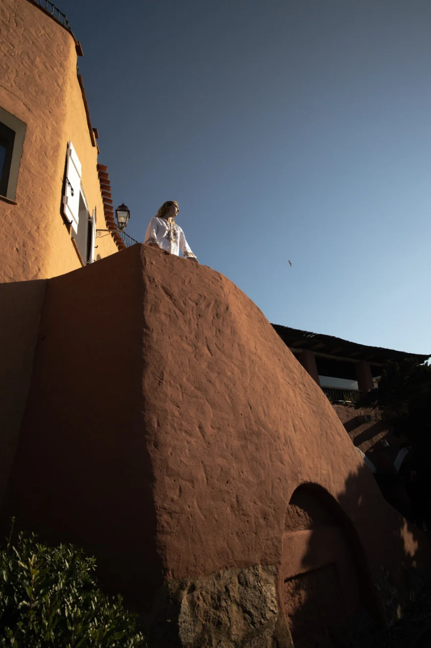 Distant figure standing on a terracotta rock beside a Mediterranean villa at dusk, Costa Smeralda Magazine editorial photographed by Ina Cenusa