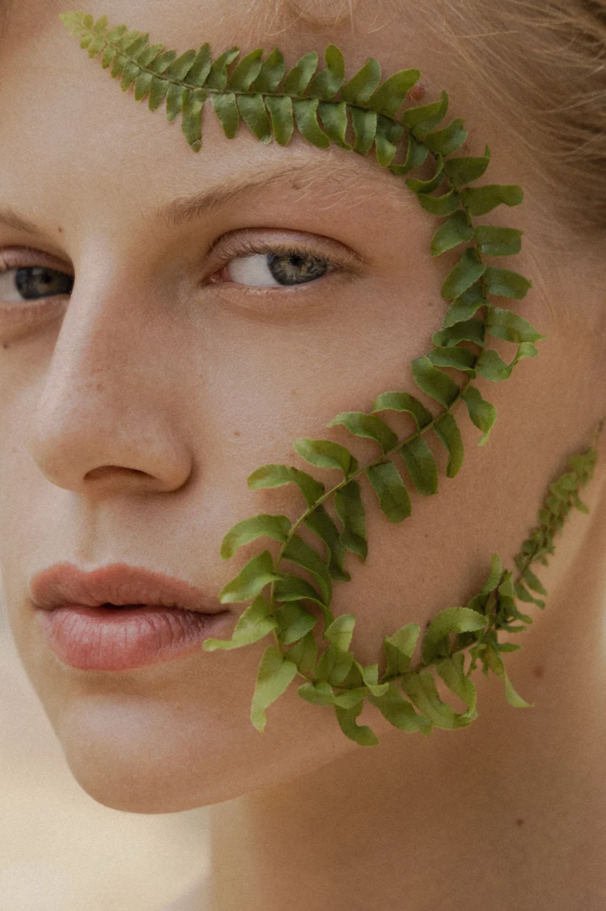 Beauty close-up with a green fern frond laid across the face, SHOT Magazine editorial photographed by Ina Cenusa