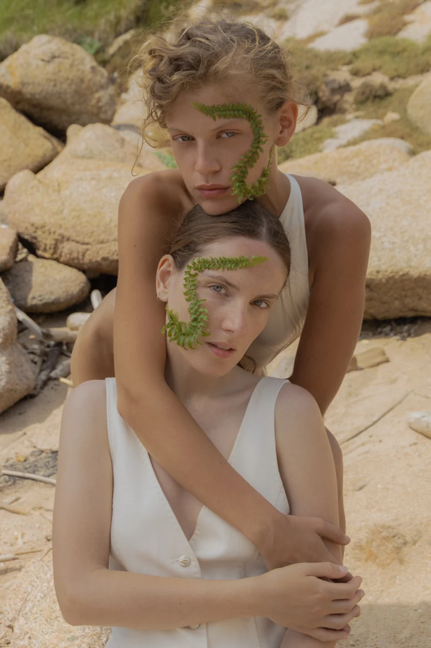 Two models embracing with fern fronds across their faces on the rocks, SHOT Magazine editorial photographed by Ina Cenusa