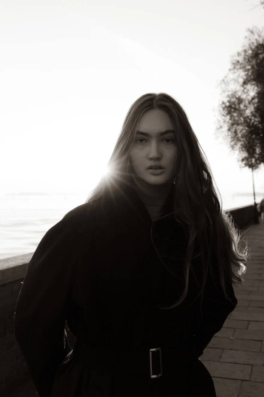 Backlit black and white portrait in a black coat by the Venetian lagoon, Daria personal project photographed by Ina Cenusa