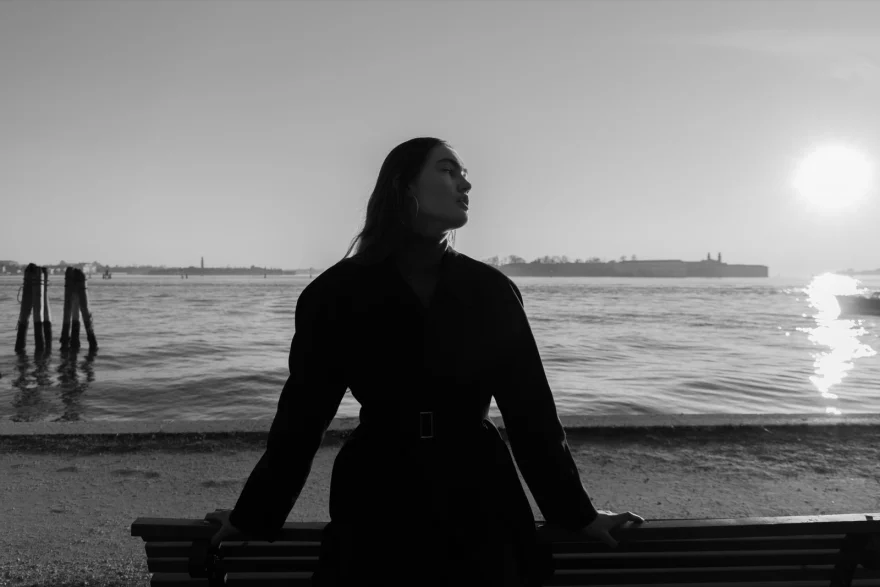 Model seated on a bench facing the lagoon at sunset, black and white, Daria personal project photographed by Ina Cenusa