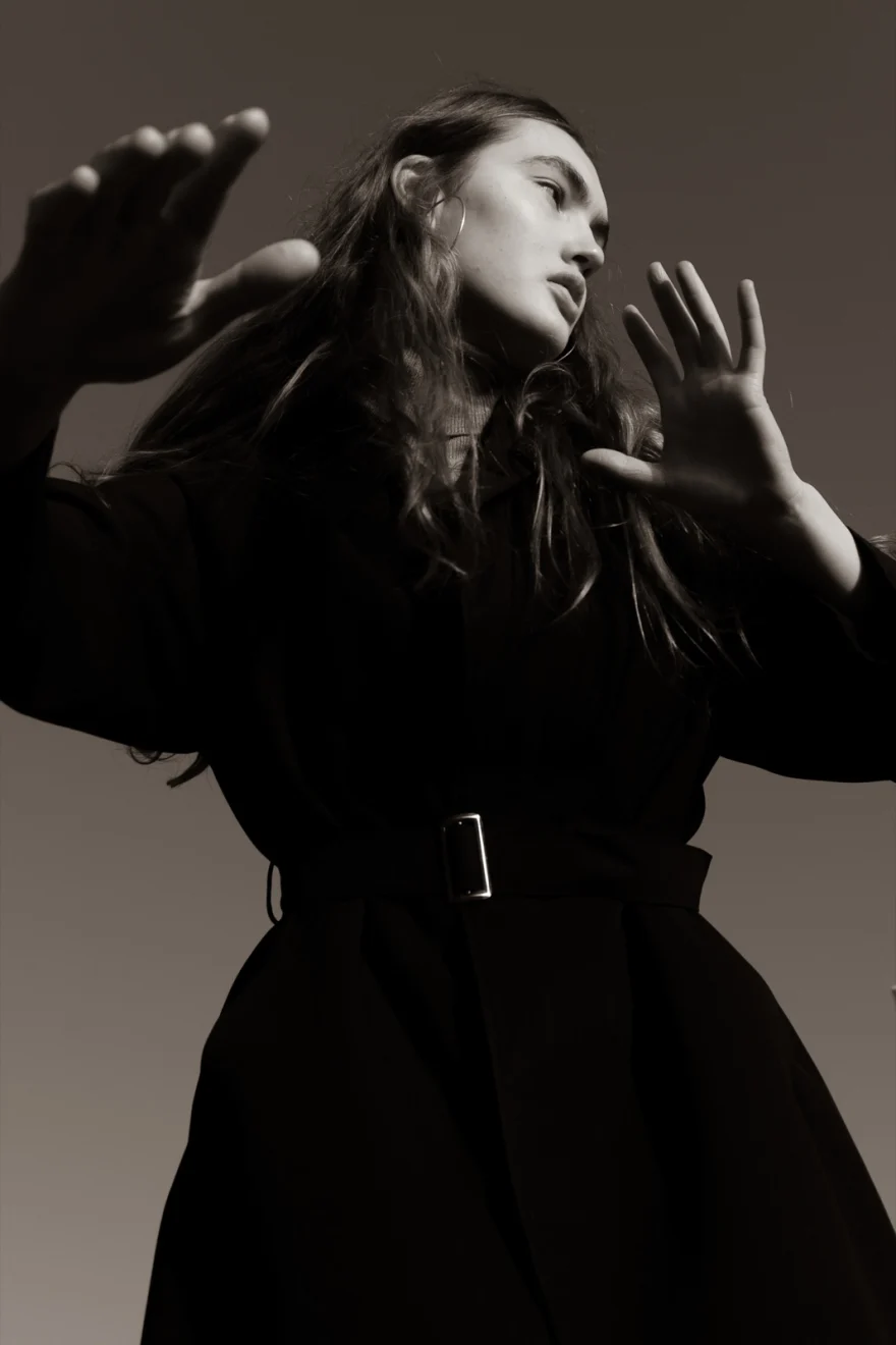 Model in a black coat with both hands raised towards the camera, Daria personal project photographed by Ina Cenusa