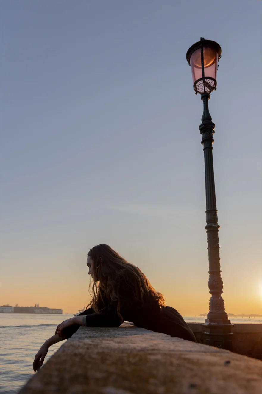 Model leaning on the waterfront wall beside a lamppost at sunset, Venice, Daria personal project photographed by Ina Cenusa