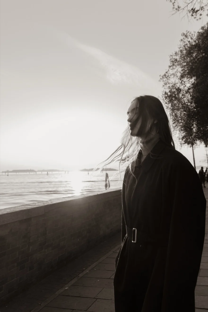 Model walking along the fondamenta with the lagoon behind, hazy backlight, Daria personal project photographed by Ina Cenusa