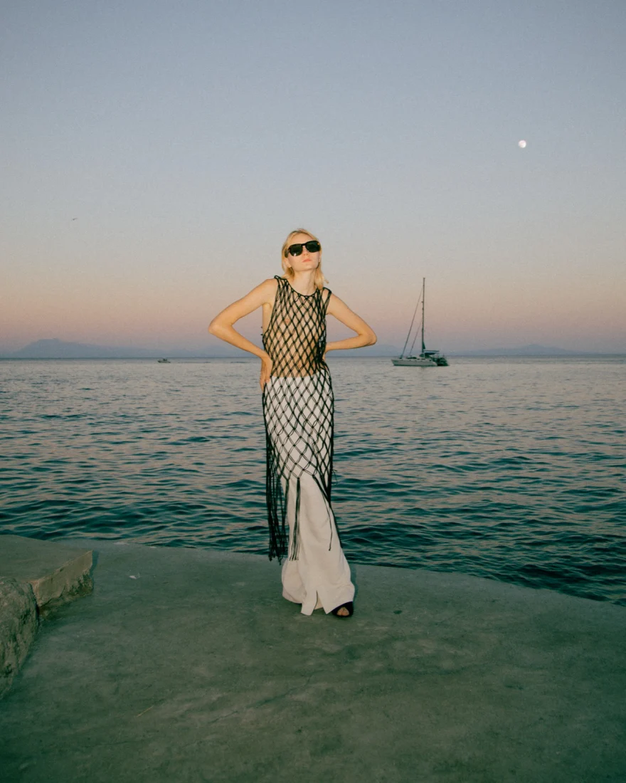 Model in a net dress with hands on hips by the sea at sunset, Amalfi coast, Luca Grassi campaign photographed by Ina Cenusa