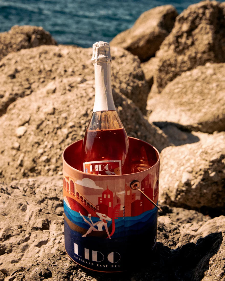Sparkling wine bottle in a branded ice bucket among seaside rocks, Lido by Canella Wine, campaign photographed by Ina Cenusa