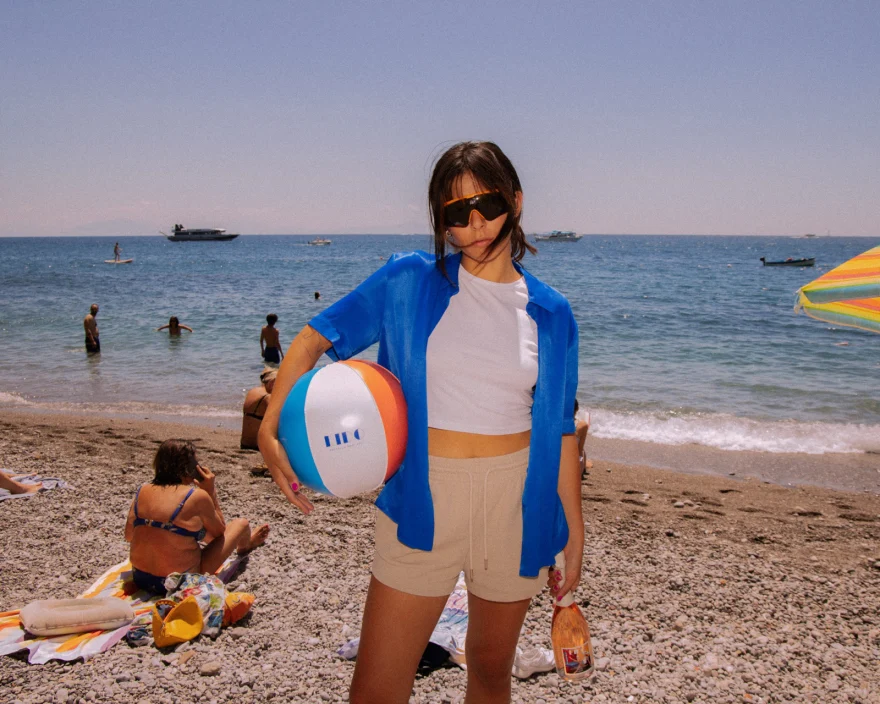 Model in a blue shirt on the beach holding a branded beach ball, Canella Wine campaign photographed by Ina Cenusa