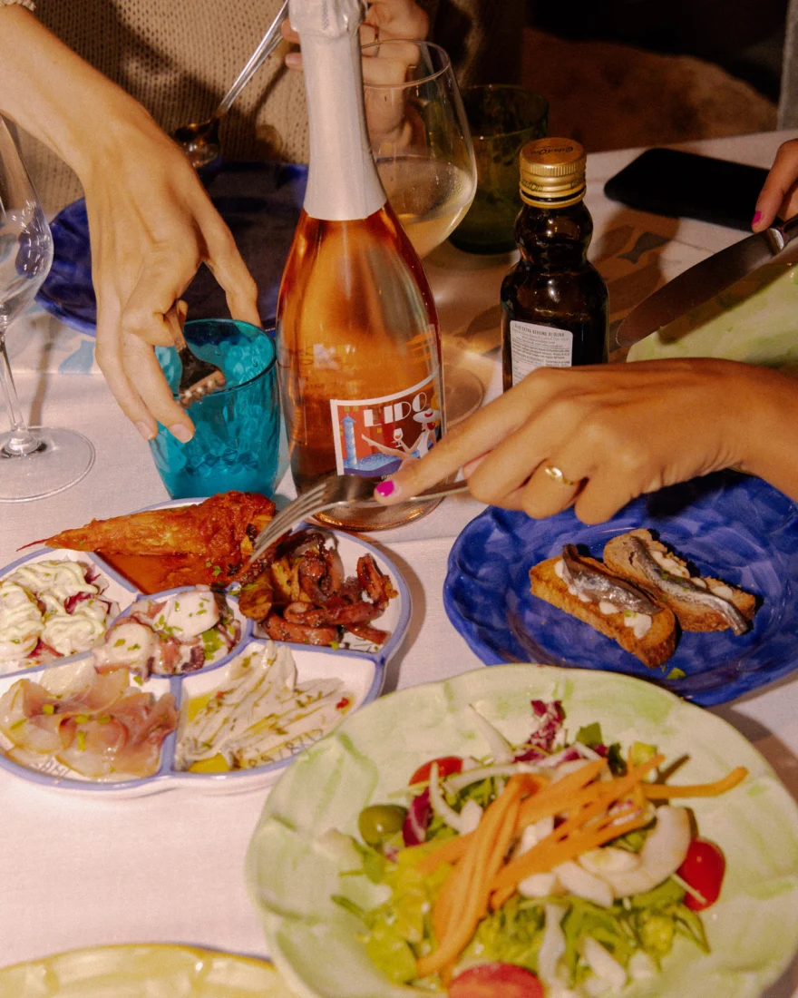 Long lunch table with a bottle of rosé among plates of food, Canella Wine campaign photographed by Ina Cenusa