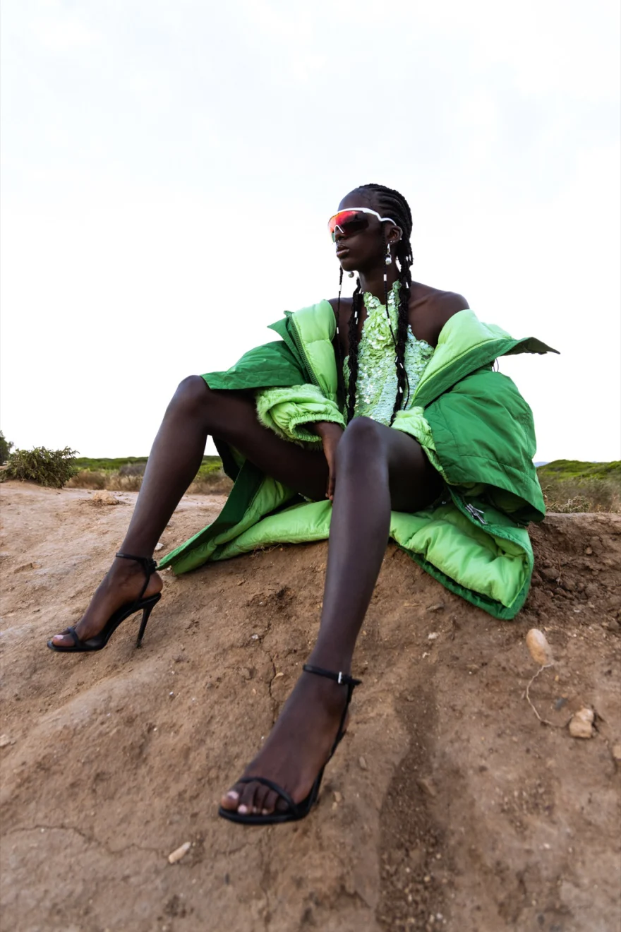 Model seated on a dirt mound wrapped in a green coat with heels, Ermanno Scervino × SHOT Magazine editorial photographed by Ina Cenusa