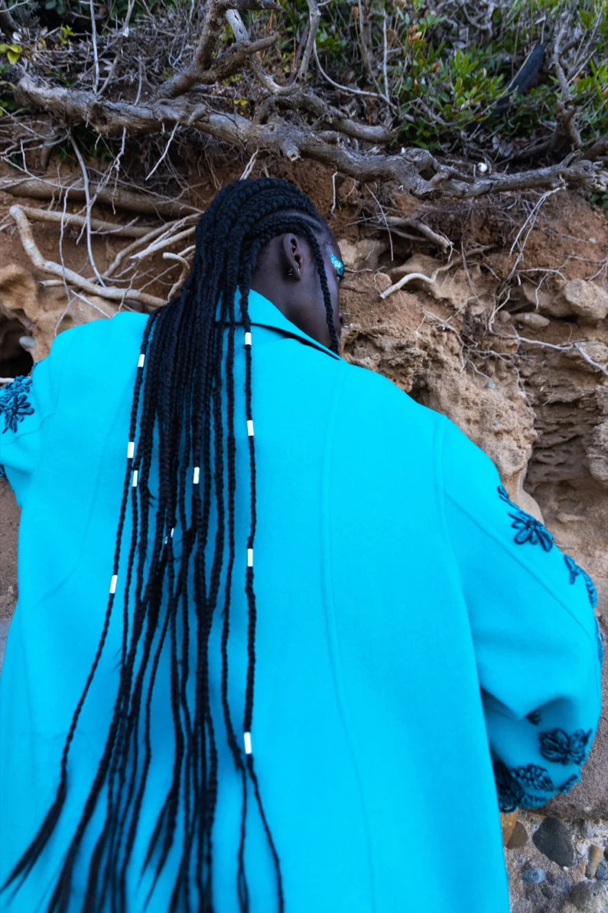 Back view of a turquoise embroidered coat against coastal rocks, Ermanno Scervino × SHOT Magazine editorial photographed by Ina Cenusa