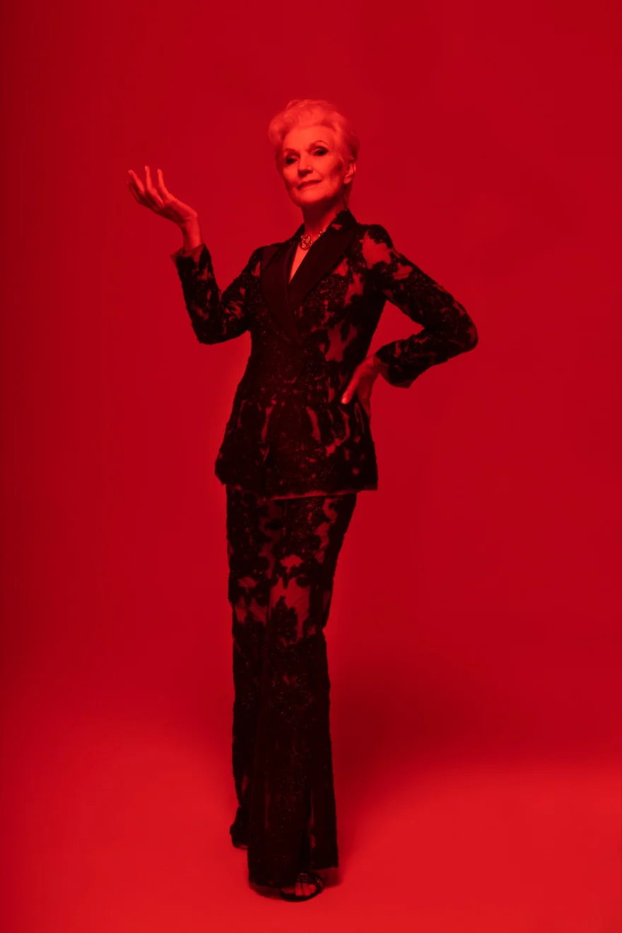 Maye Musk in a black lace tailored suit with one hand raised, bathed in red light, SHOT Magazine campaign photographed by Ina Cenusa