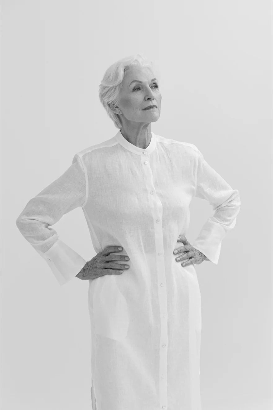 Maye Musk in a long white shirt dress against a pale grey ground, SHOT Magazine campaign photographed by Ina Cenusa