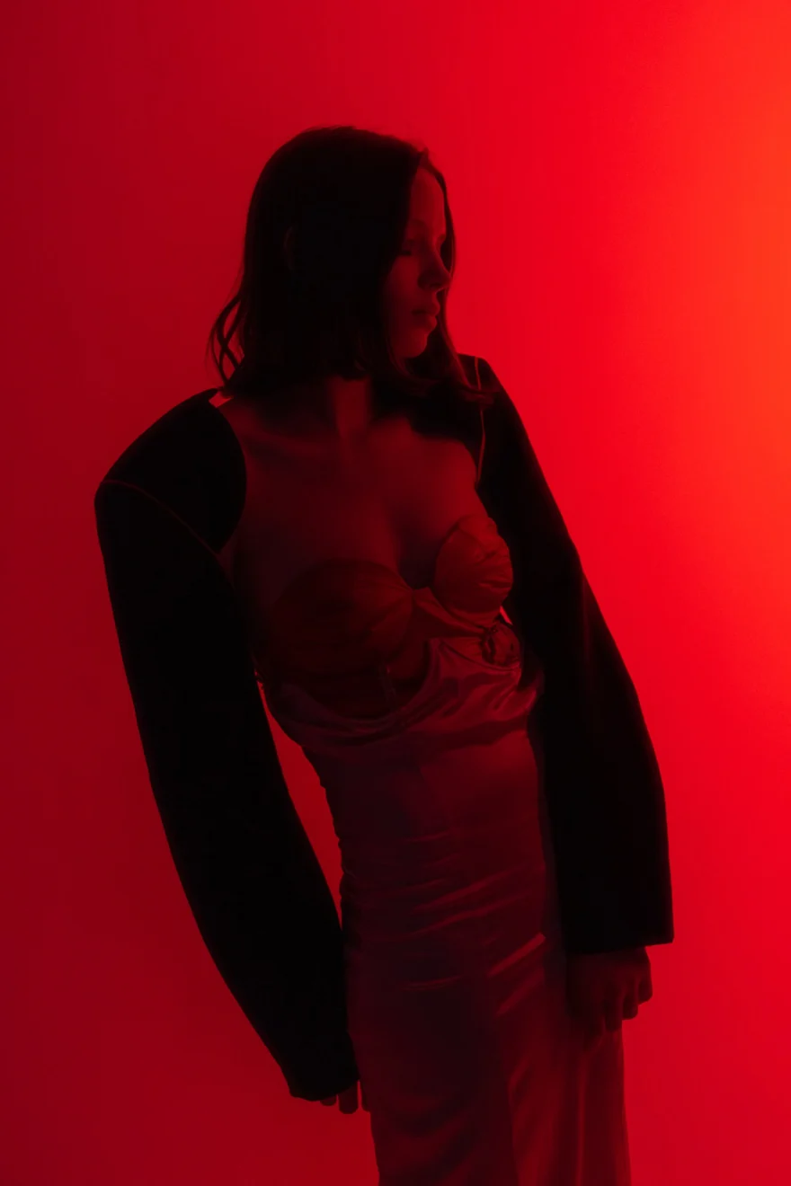 Model in a black jacket over a pale slip dress against a deep red backdrop, Sabina personal project photographed by Ina Cenusa