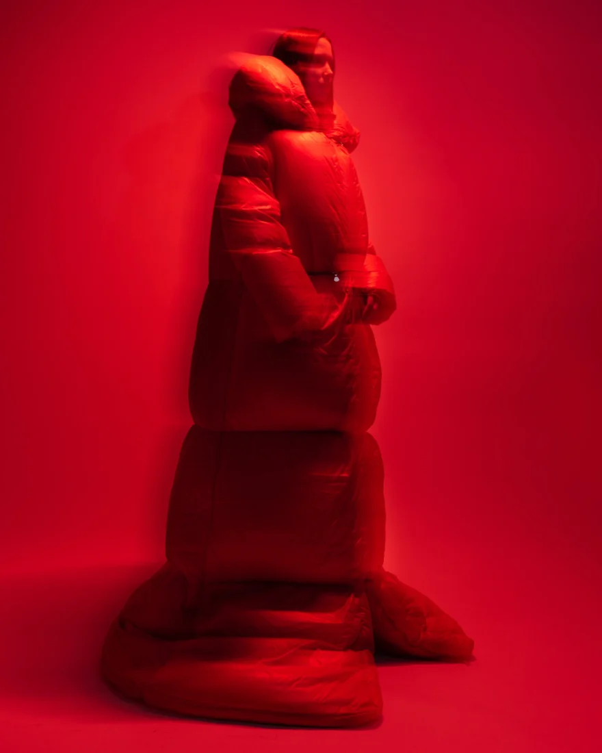 Model wrapped in a sculptural padded coat under saturated red light, Sabina personal project photographed by Ina Cenusa