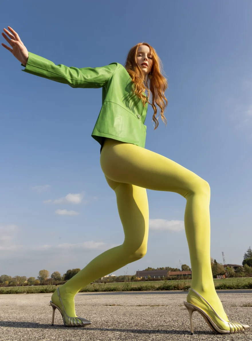Model in yellow tights and a green jacket striding on the tarmac, Trasparenze campaign photographed by Ina Cenusa