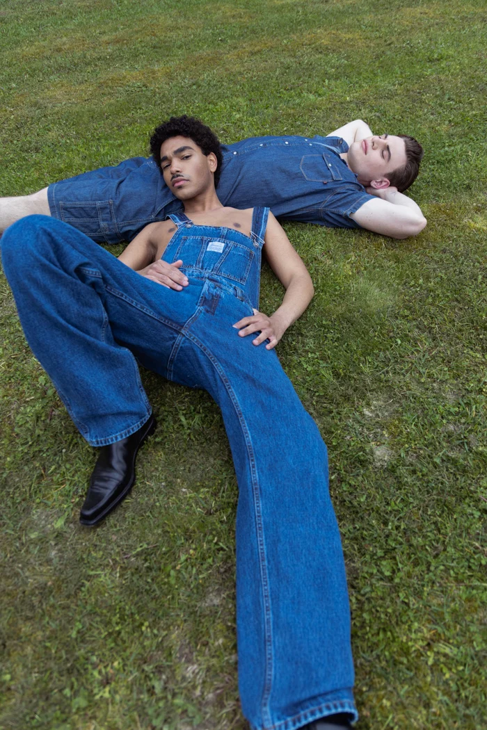 Two models in denim dungarees lying head to head on the grass, Carrera Jeans campaign photographed by Ina Cenusa