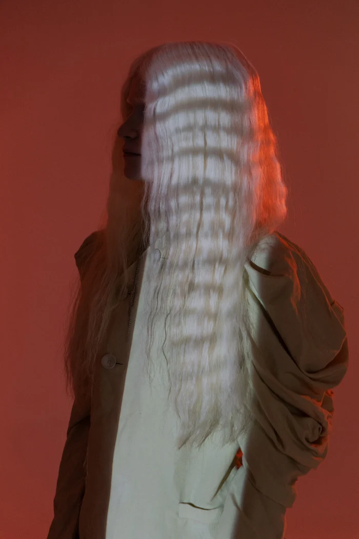 Long pale hair falling over the face against an orange background, SHOT Magazine editorial photographed by Ina Cenusa