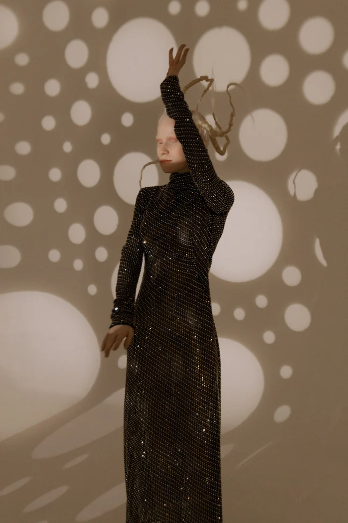 Model in a long sequinned dress with arms raised under projected light, SHOT Magazine editorial photographed by Ina Cenusa