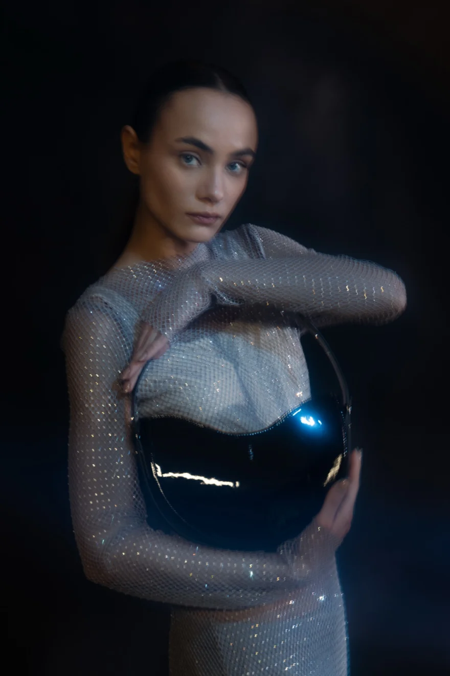 Model in a crystal mesh dress holding a black domed bag, Noesi campaign photographed by Ina Cenusa