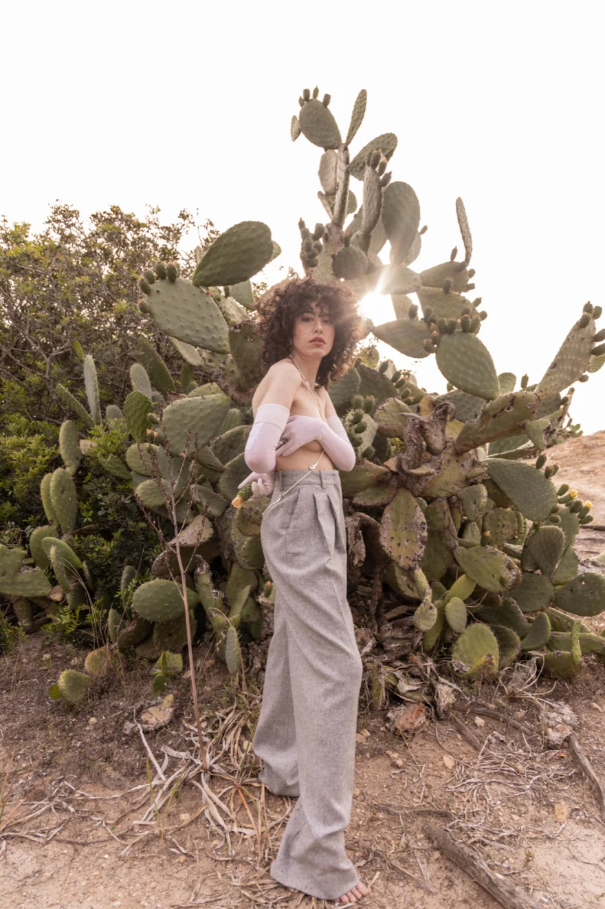 Model backlit among prickly pear cactus in wide grey trousers, SHOT Magazine editorial photographed by Ina Cenusa