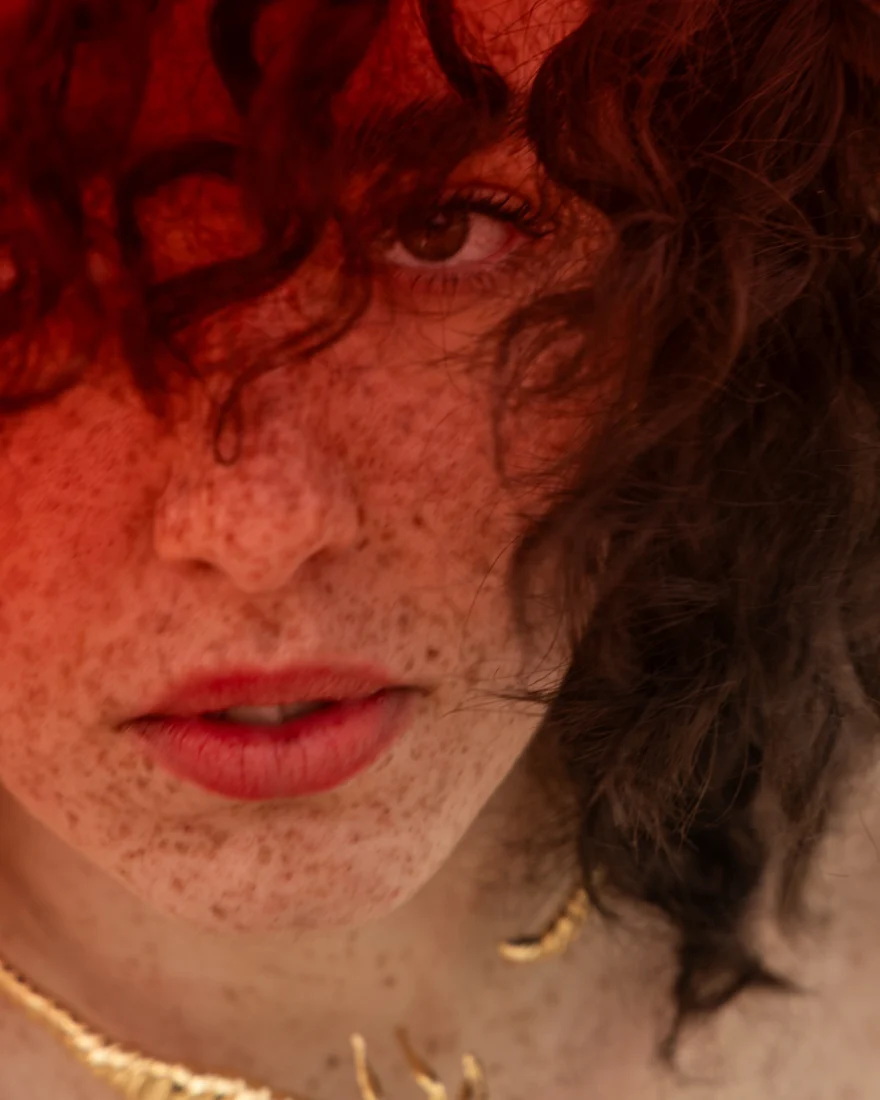 Beauty close-up of freckled skin and curly hair in warm red light, SHOT Magazine editorial photographed by Ina Cenusa