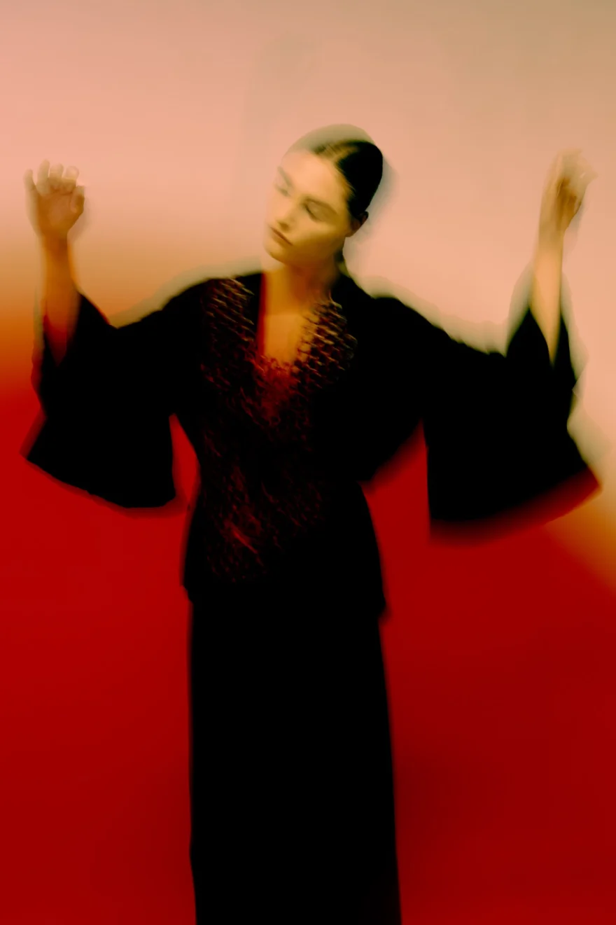 Motion-blurred portrait of a model in a black kimono-sleeve look with arms raised, SHOT Magazine editorial photographed by Ina Cenusa