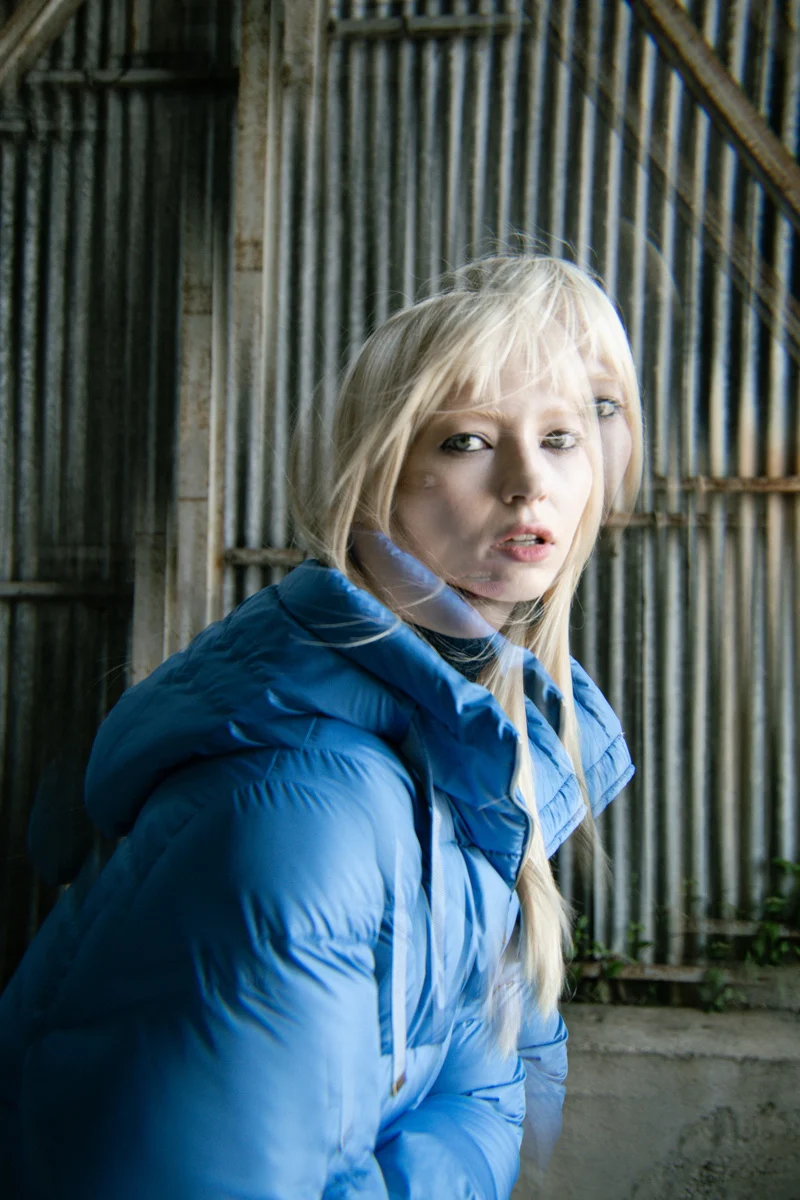 Model in a blue padded jacket against corrugated metal, Mabrun campaign photographed by Ina Cenusa
