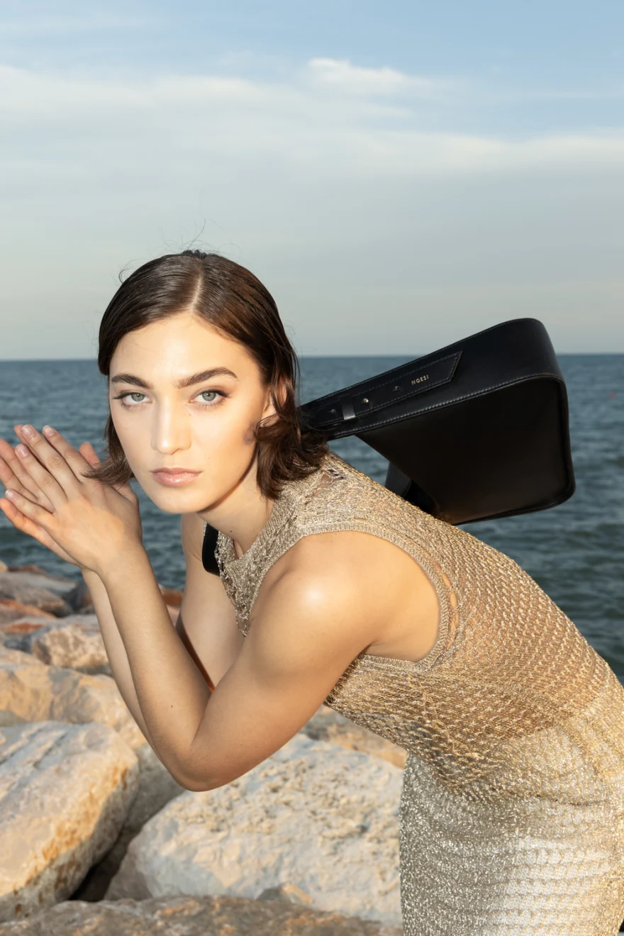 Model in a knitted dress on the rocks with a black bag, Noesi campaign photographed by Ina Cenusa