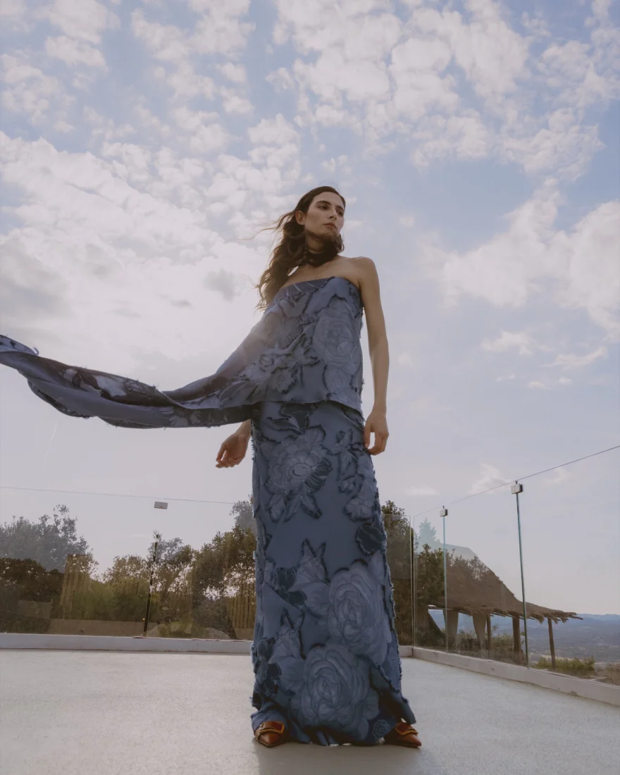 Model in a blue floral gown with fabric lifted by the wind against the sky, SHOT Magazine editorial photographed by Ina Cenusa
