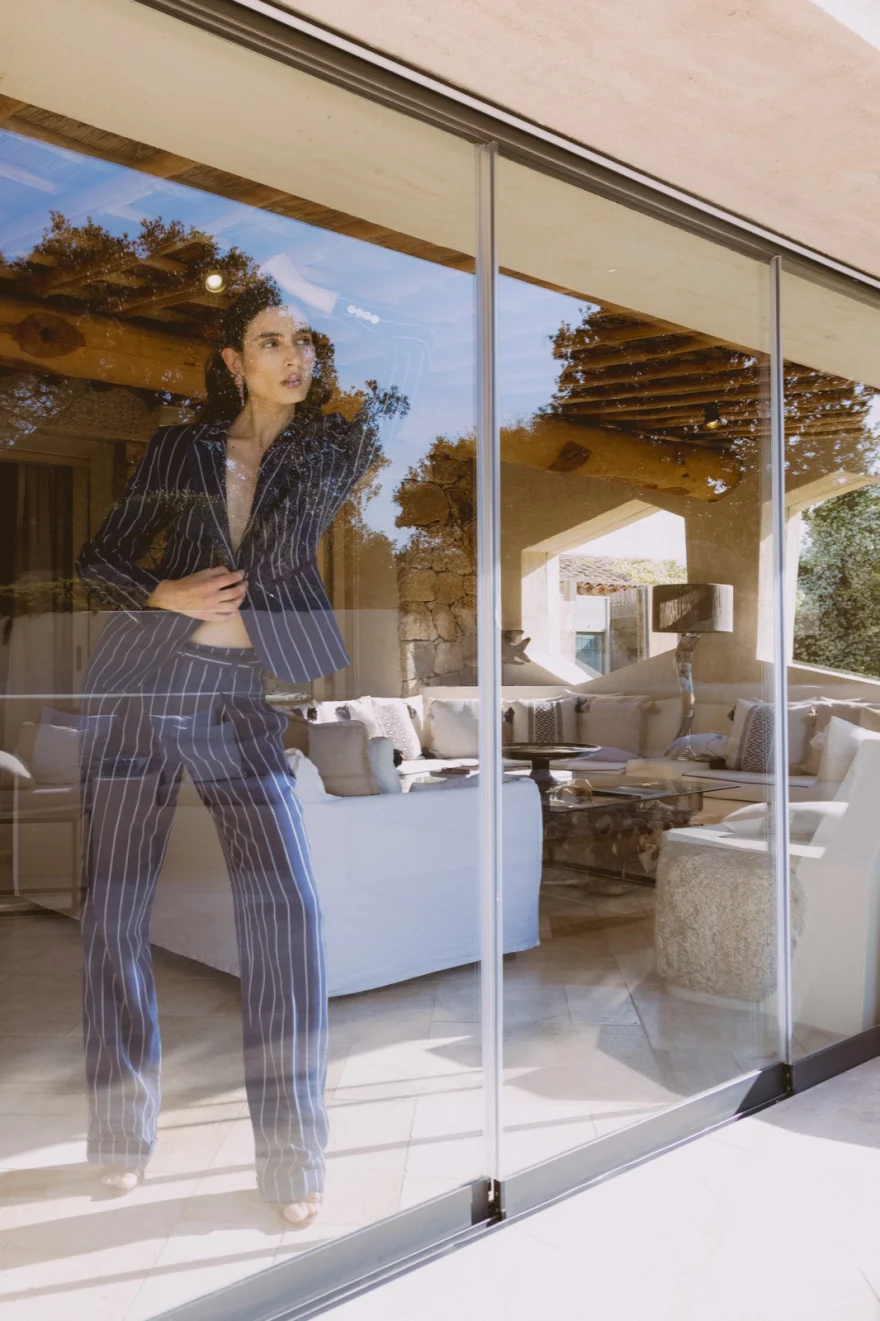 Model in a pinstripe suit seen through a glass door with reflections of the terrace, SHOT Magazine editorial photographed by Ina Cenusa