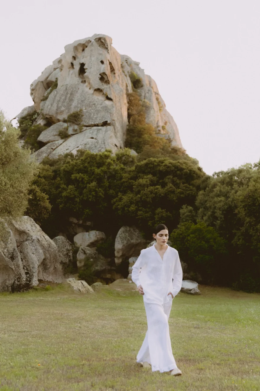 Model in a white look walking a meadow below a granite outcrop, SHOT Magazine editorial photographed by Ina Cenusa