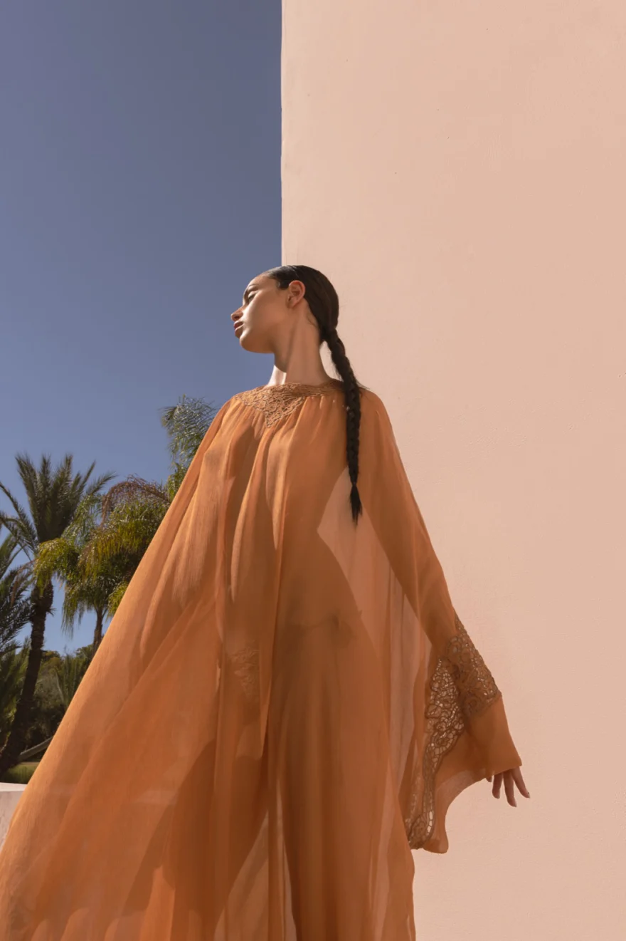 Model in a camel cape caught by the wind against a blue sky, Ermanno Scervino campaign in Marrakech, Morocco, photographed by Ina Cenusa