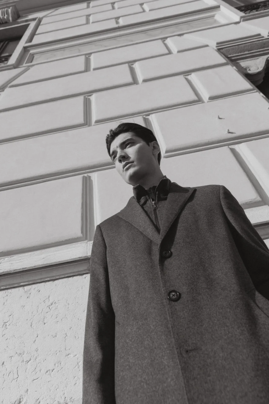 Low-angle portrait in a grey overcoat against tiled architecture, Mabrun campaign photographed by Ina Cenusa