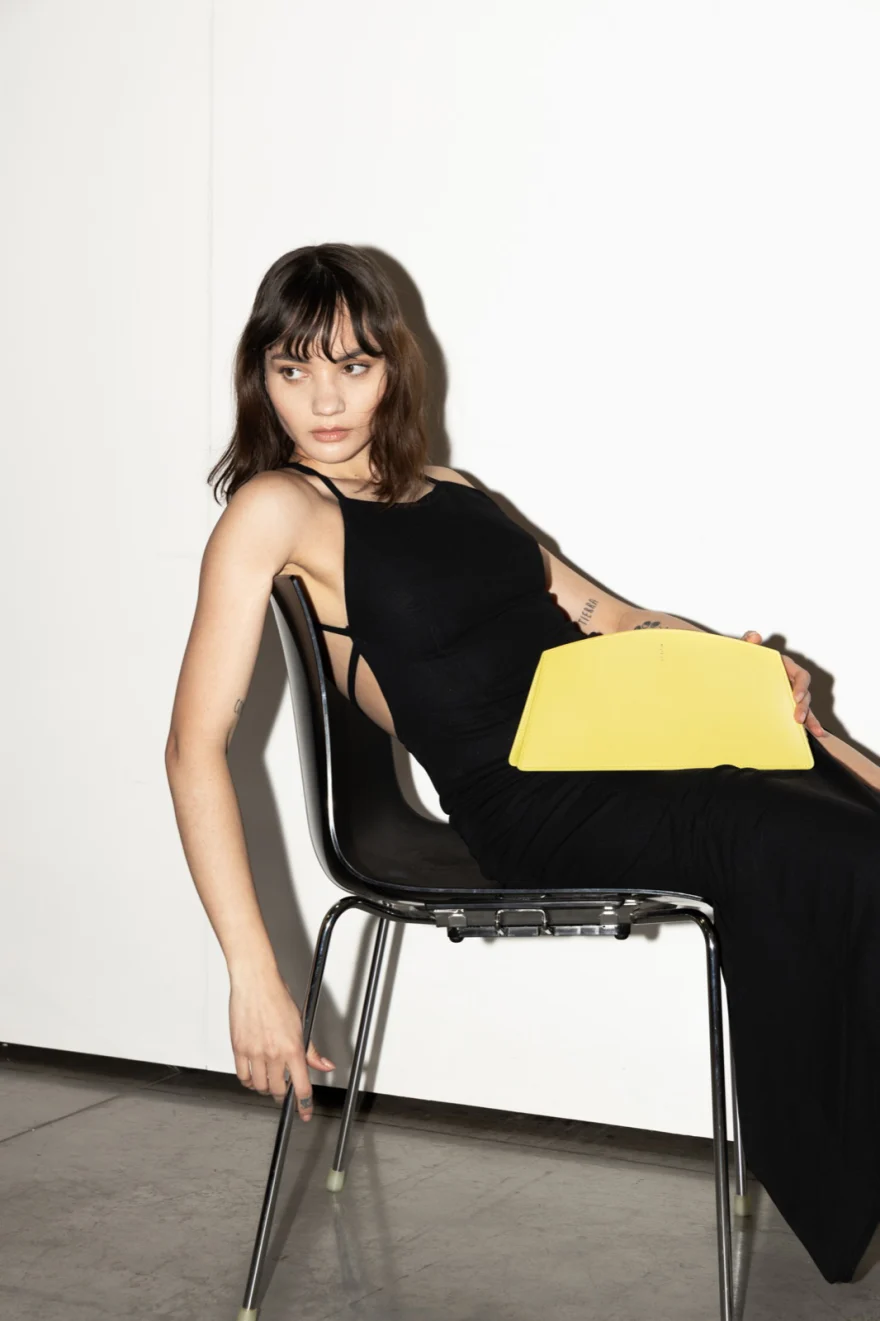 Model seated on a black chair holding a yellow clutch, Noesi campaign photographed by Ina Cenusa
