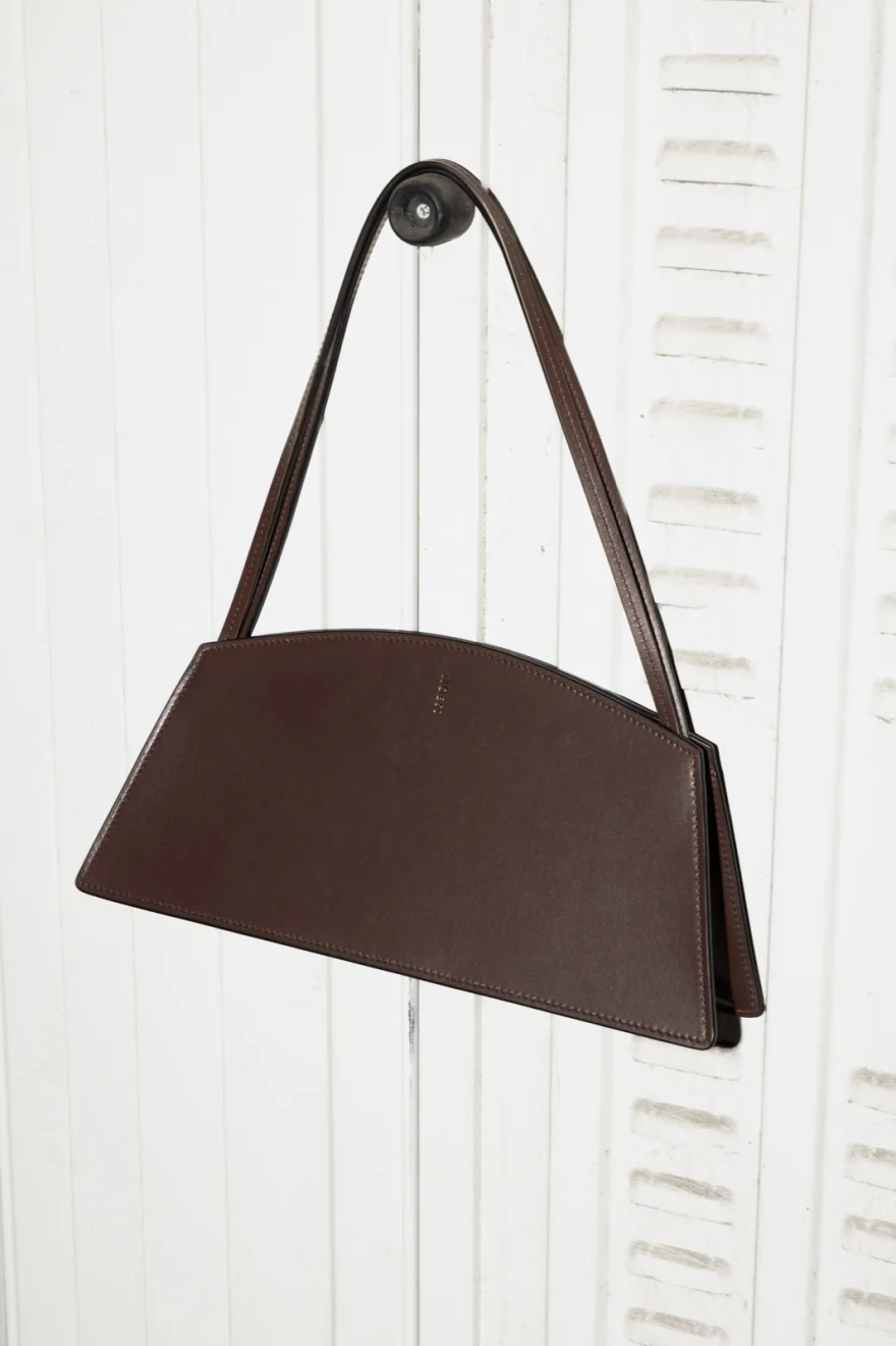 Still life of a brown leather shoulder bag hung on a white wall, Noesi campaign photographed by Ina Cenusa