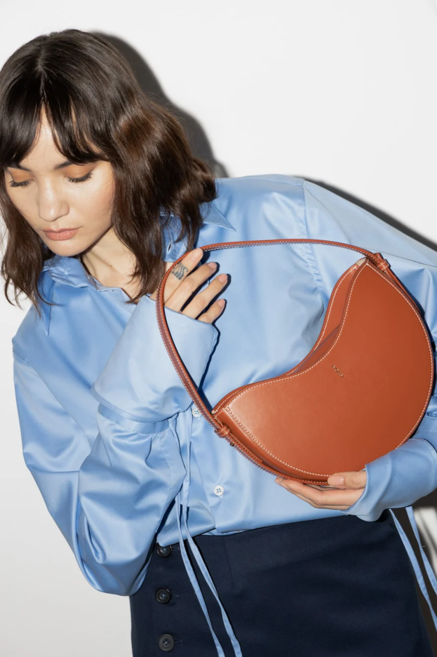Model in a blue shirt with a tan crescent shoulder bag, Noesi campaign photographed by Ina Cenusa