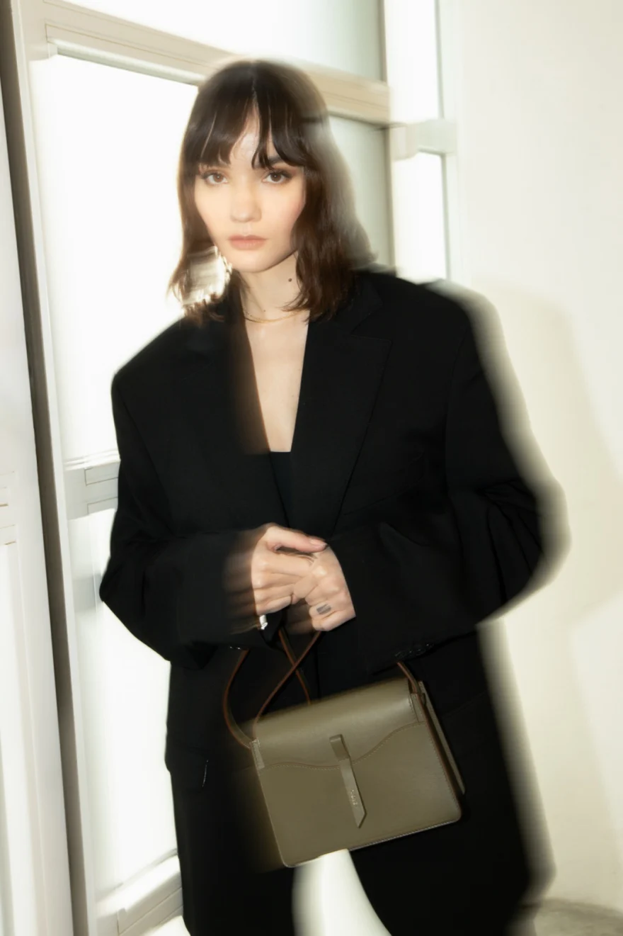 Model in a black suit holding an olive shoulder bag, Noesi campaign photographed by Ina Cenusa